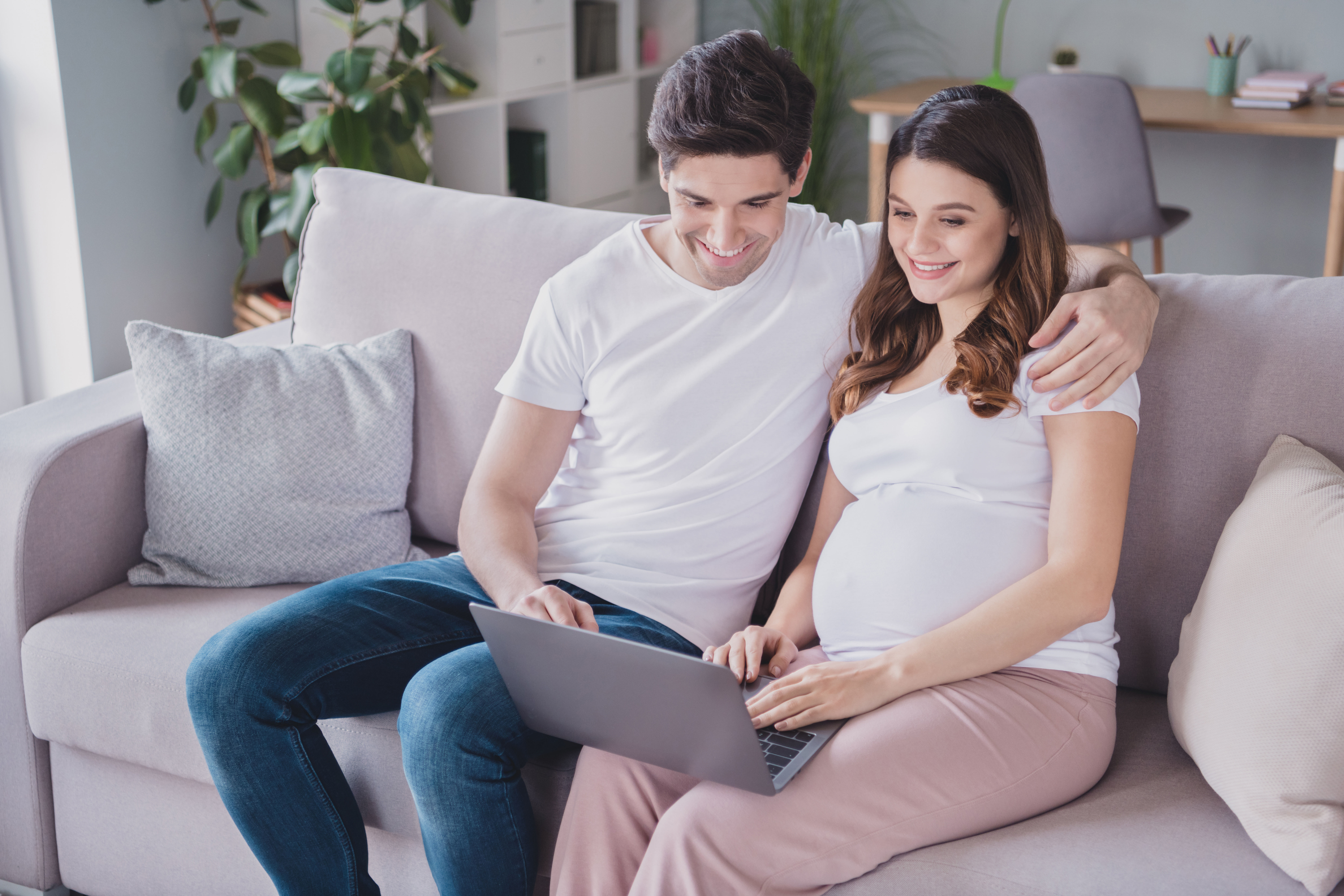 pregnant woman and man on couch looking at computer virtual class prenatal