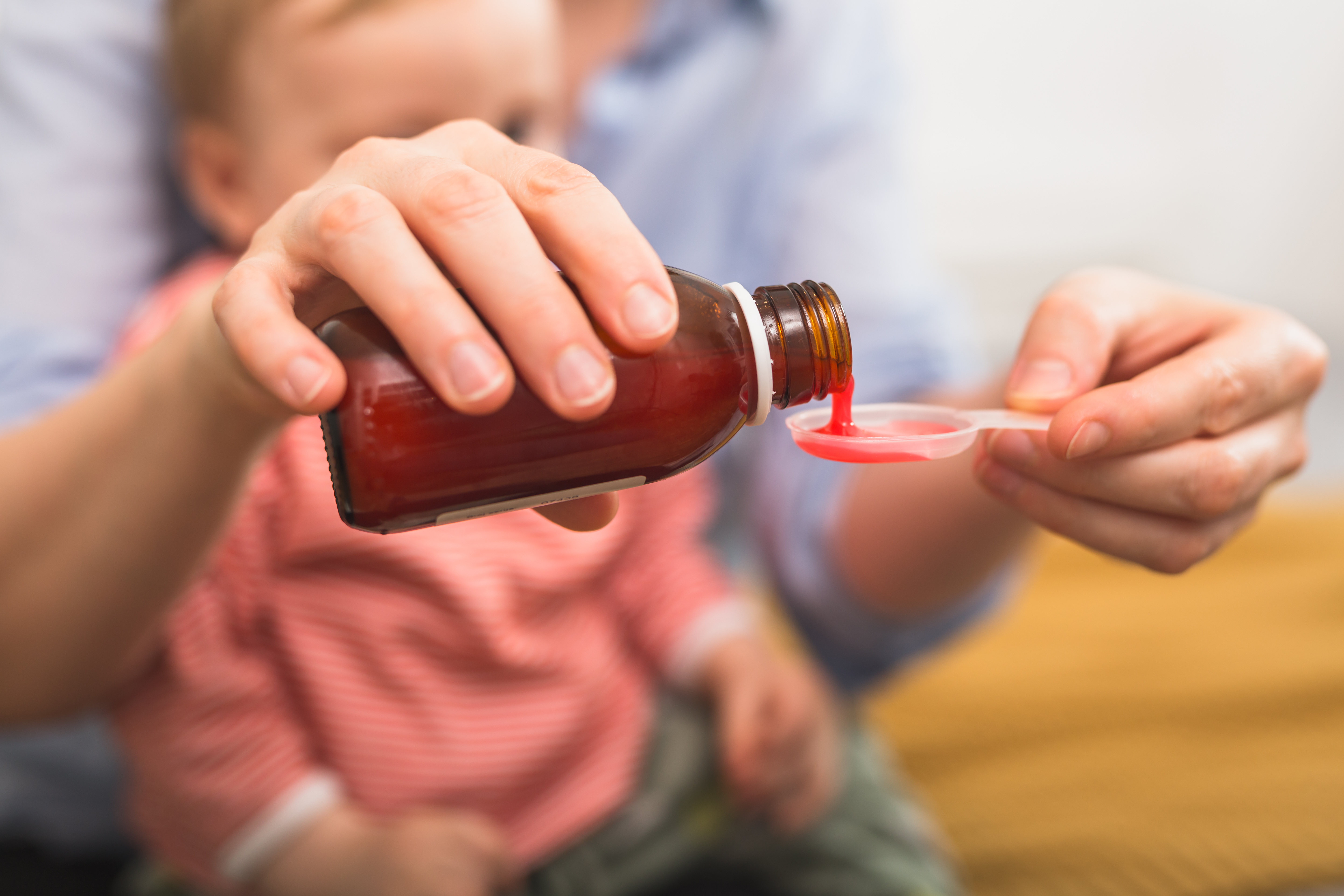 parent pouring liquid medication while kid watches