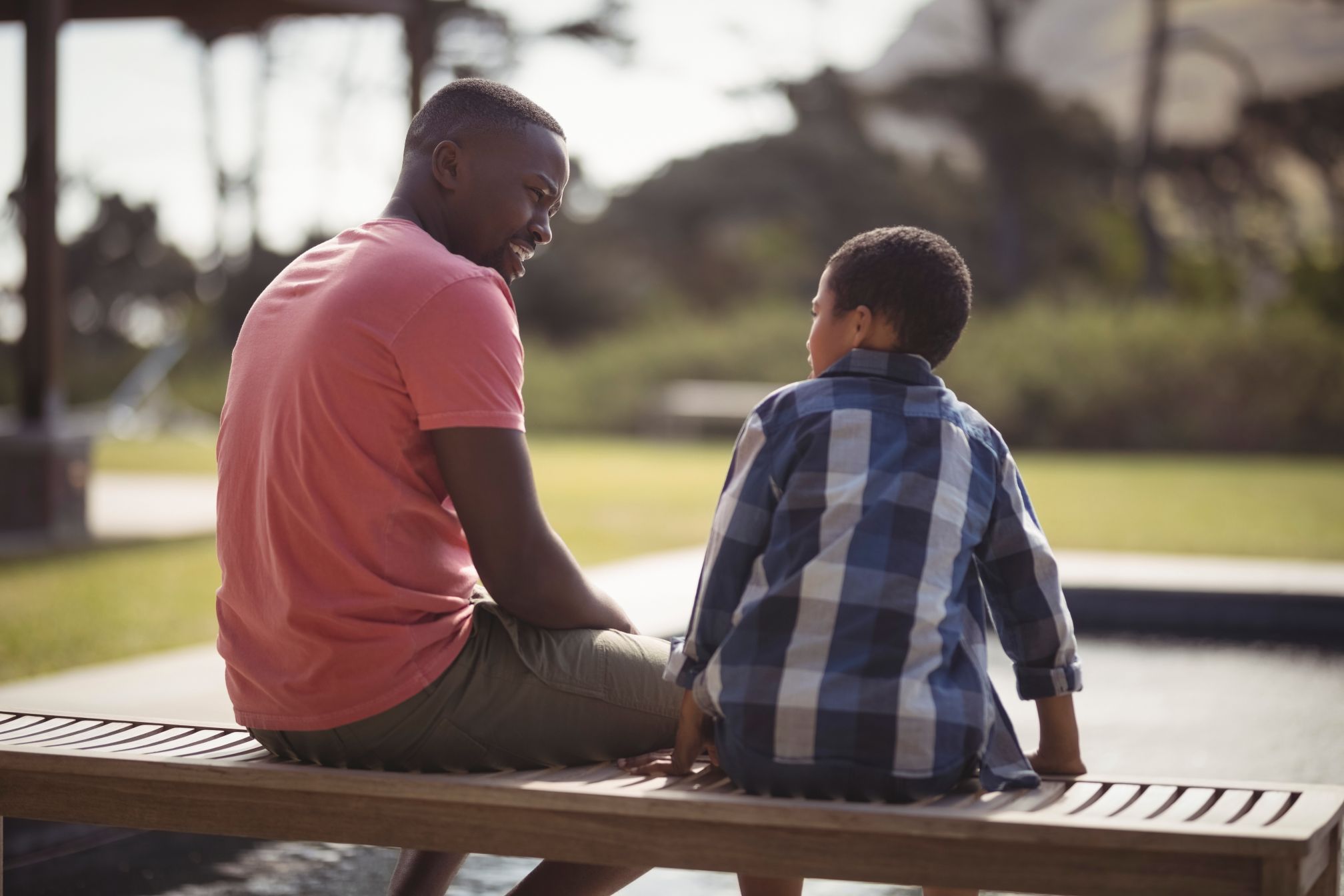 dad sitting on bench with school age son talking listening parent child communicaton