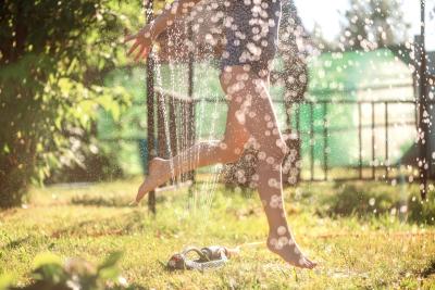 kid running through sprinkler summer heat safety prevention water