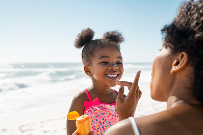 mom applying sunscreen on dark skinned black daughter at the beach tips summer spring sun prevention skin